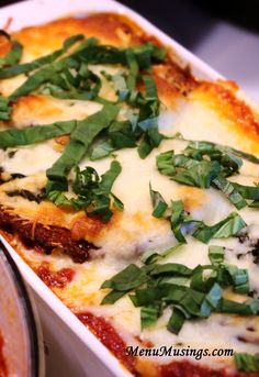 a casserole dish with spinach and cheese on top, next to a pot of sauce