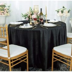 the table is set with black linens and white chairs