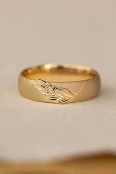 a gold wedding band with leaves on the side, sitting on top of a piece of paper