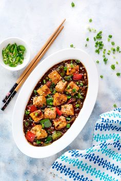 a white bowl filled with meat and vegetables next to chopsticks on a table