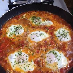 a pizza with eggs and cheese on it in a black pan sitting on top of a stove