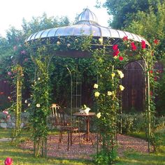 a gazebo with roses growing over it and two chairs around the table in front