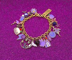 My Favorite Color Is Purple Bracelet These one-of-a-kind favorite color bracelets are for the Adventurus Purple. Every possible purple charm and bead is available on these two bracelets (Sold Separately). Charms of various sizes and themes are presented, and a mix of bead dangles is placed among the cute green charms. Each bracelet includes a word charm that states the purpose of the jewelry piece. The fun-loving Lucinda Calligraphy font word charm is laser engraved on the rectangle, and it reads,  "My favorite color is Purple." The stainless Steel Gold-Plated Charm measures 25 x 9mm. Two available styles The large charms bracelet has 15 enamel charms and 5 beads dangles of differing materials. The largest charm is 25mm, and the smallest is 9mm. (Photos 1-5) The small charm bracelet has 15 Themed Multicolor Bracelet Jewelry, Color Bracelets, Charm Bracelet Gold, Green Charms, Bead Dangles, Jewelry Purple, Gold Chain Bracelet, Color Bracelet, Purple Bracelet