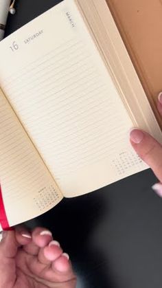 a person is holding an open notebook in their left hand while sitting at a desk