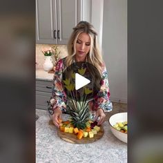 a woman standing in front of a bowl of fruit on top of a counter next to a pineapple