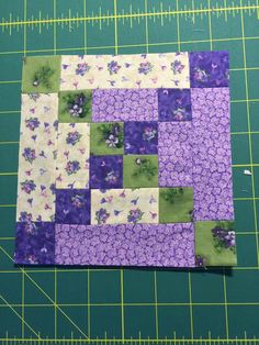 a piece of fabric is laying on a cutting board with purple and green squares in the middle