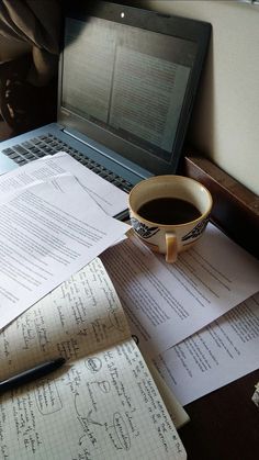 a cup of coffee sitting on top of papers next to a laptop computer