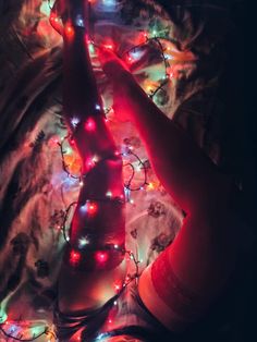 a woman laying on top of a bed with christmas lights all over her body and legs