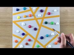 someone is painting on a piece of white paper with colorful dots and lines in the background