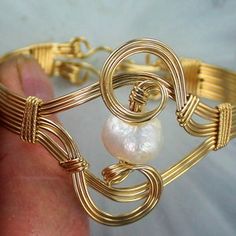 a hand holding a gold wire bracelet with white pearls on it's end and an eye shaped bead in the middle