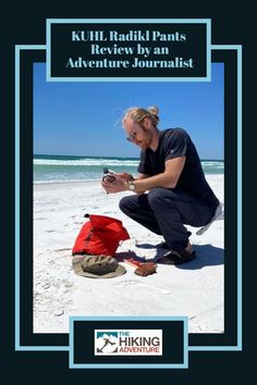 a man kneeling down next to a red backpack on top of a white sandy beach