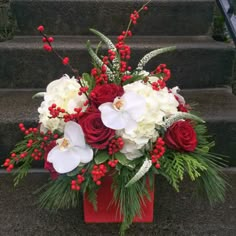 red and white flowers are in a vase on the steps with greenery, berries, and pine cones