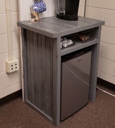 a coffee maker sitting on top of a wooden table next to a trash can and garbage can