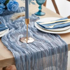 a table set with blue and white plates, silverware, and candlesticks