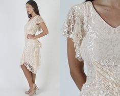 "Vintage 80s sheer ivory floral lace dress. V neck wrap style bodice with fluttery sleeves. Gathered and fitted waist with sweeping, tulip hi lo skirt. Dress is lined and zips up the back. size estimate: S shoulders: 17.5\" bust: 30\" waist: 28\" hips: 30\" total length: 35\"-42\" Model is 5'9\" and measures 33\" bust, 25\" waist, 33\" hips. Belts/accessories are not included unless noted in the description." Fitted V-neck Lace Dress For Wedding Guest, Fitted Lace Dress With Ruffles For Wedding Guests, Cream Fitted Lace Dress With V-neck, Fitted V-neck Lace Wedding Dress, Fitted Short Sleeve Lace Dress With Delicate Lace, Delicate Lace Fitted Dress With Short Sleeves, Fitted Short Sleeve Delicate Lace Dress, Beige V-neck Lace Dress For Party, Vintage Lace V-neck Dresses