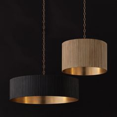 two black and gold lamps hanging from chains on a dark wall, one with a beige shade