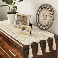 a white crocheted table runner with tassels and a photo frame on it