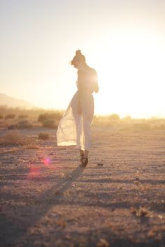 a woman is walking in the desert at sunset