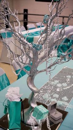 a table topped with a silver tree filled with gift wrapped in blue and white paper