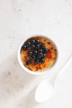 a white bowl filled with blueberries on top of a table next to a spoon