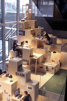 people are sitting at desks in a room with shelves and boxes on the floor