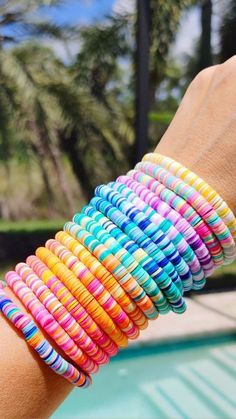 a woman's arm with multicolored bracelets next to a swimming pool