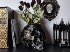 there is a skull vase with flowers in it on the table next to books and candles