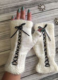 a woman's hand wearing white knitted gloves with black laces and bows