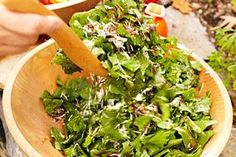 a person holding a wooden bowl filled with green vegetables and salad dressing on top of a table