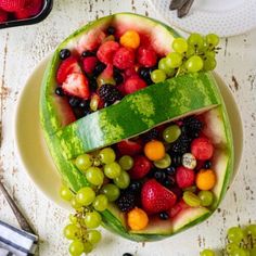 a watermelon shaped like a boat filled with berries and other fruits on top of a white table