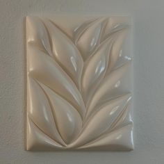 a white square tile with a leaf design on the front and back of it's face