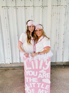 two women standing next to each other holding a pink sign