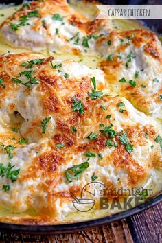 a casserole dish with cheese and parsley on top, sitting on a wooden table