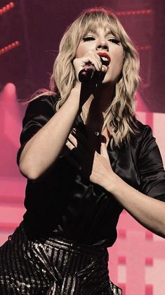 taylor swift performing on stage with her hands in the air while wearing a black top