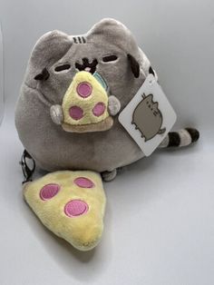 a gray stuffed animal with pink and yellow patches on it's face sitting next to a piece of food