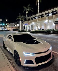 a white chevrolet camaro parked on the side of the road at night with palm trees in the background