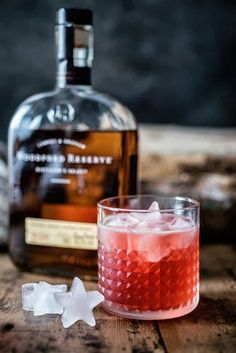 a glass filled with ice next to a bottle of alcohol on top of a wooden table