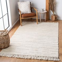 a white rug with fringes on the floor in front of a chair and window