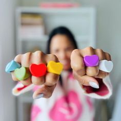 a woman is holding four small heart shaped magnets in her hands and pointing them at the camera