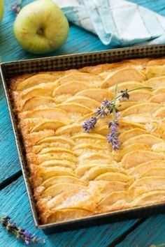 an apple pie is in a baking pan on a blue wooden table with lavender sprigs