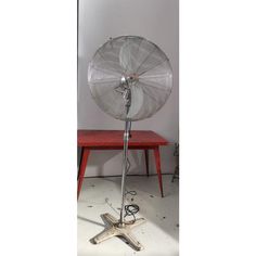 a metal fan sitting on top of a wooden table next to a red bench and white wall