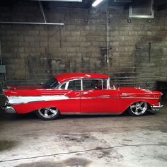 an old red and white car parked in a garage next to a brick wall,