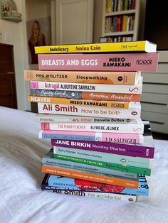 a stack of books sitting on top of a bed in front of a bookcase