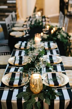 a long table with black and white striped linens, candles and greenery on it