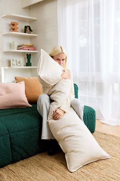 a woman sitting on top of a green couch holding a pillow in front of her face