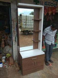 a man standing in front of a wooden dresser with a mirror on top of it