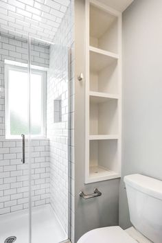 a white toilet sitting next to a walk in shower under a bathroom window with open shelving