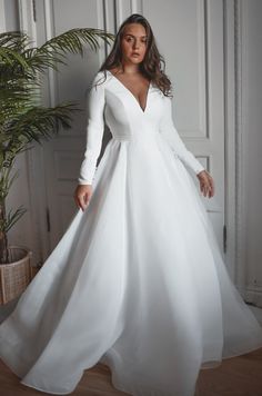 a woman wearing a white wedding dress with long sleeves and a deep v - neckline