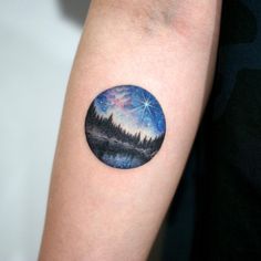 a person with a small tattoo on their arm that has a forest scene in it