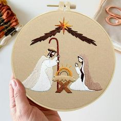 a hand is holding up a embroidery hoop with a nativity scene on it